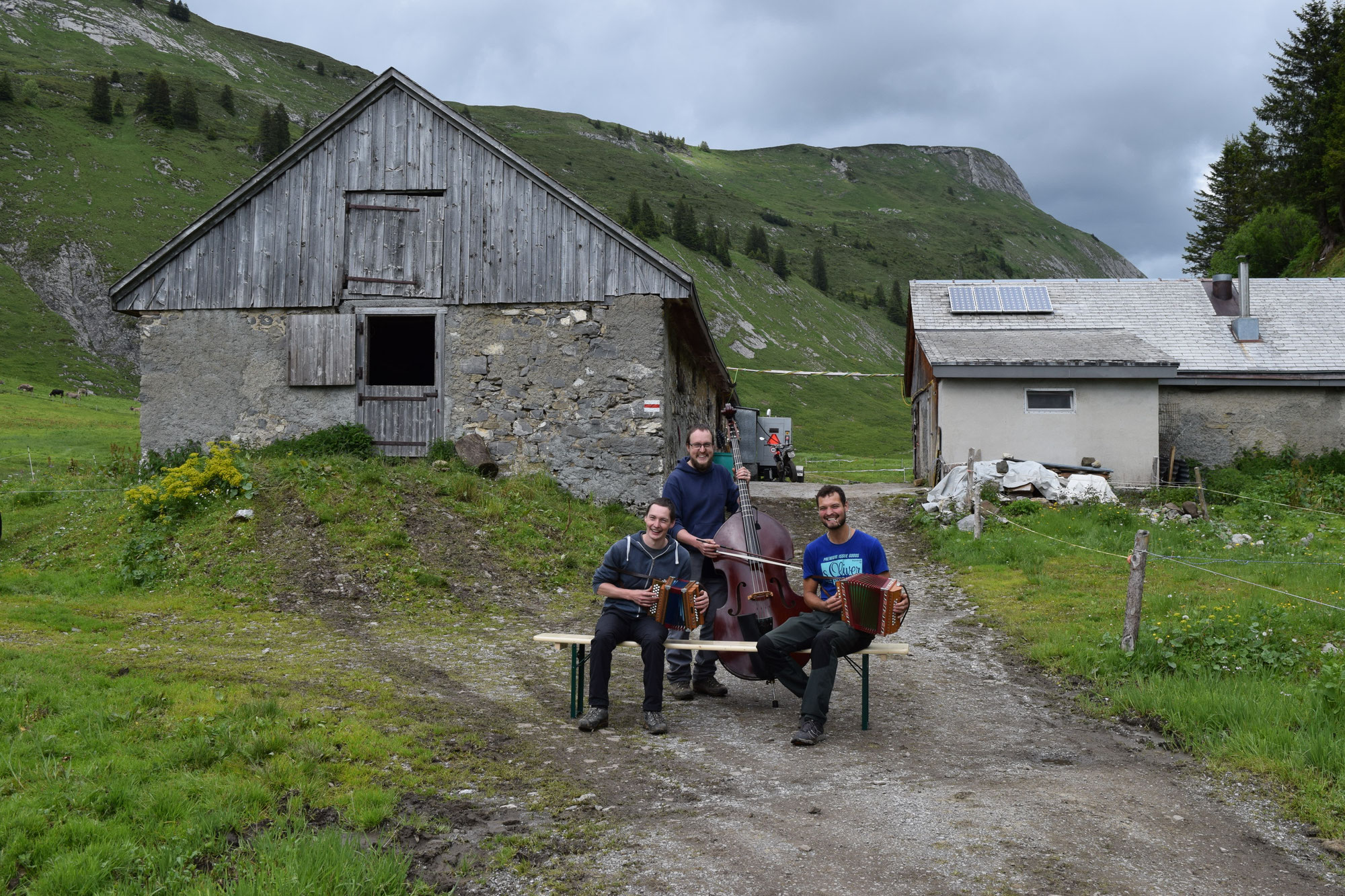 Das Trio mit Instrumenten auf einer Bank vor einer Alphütte