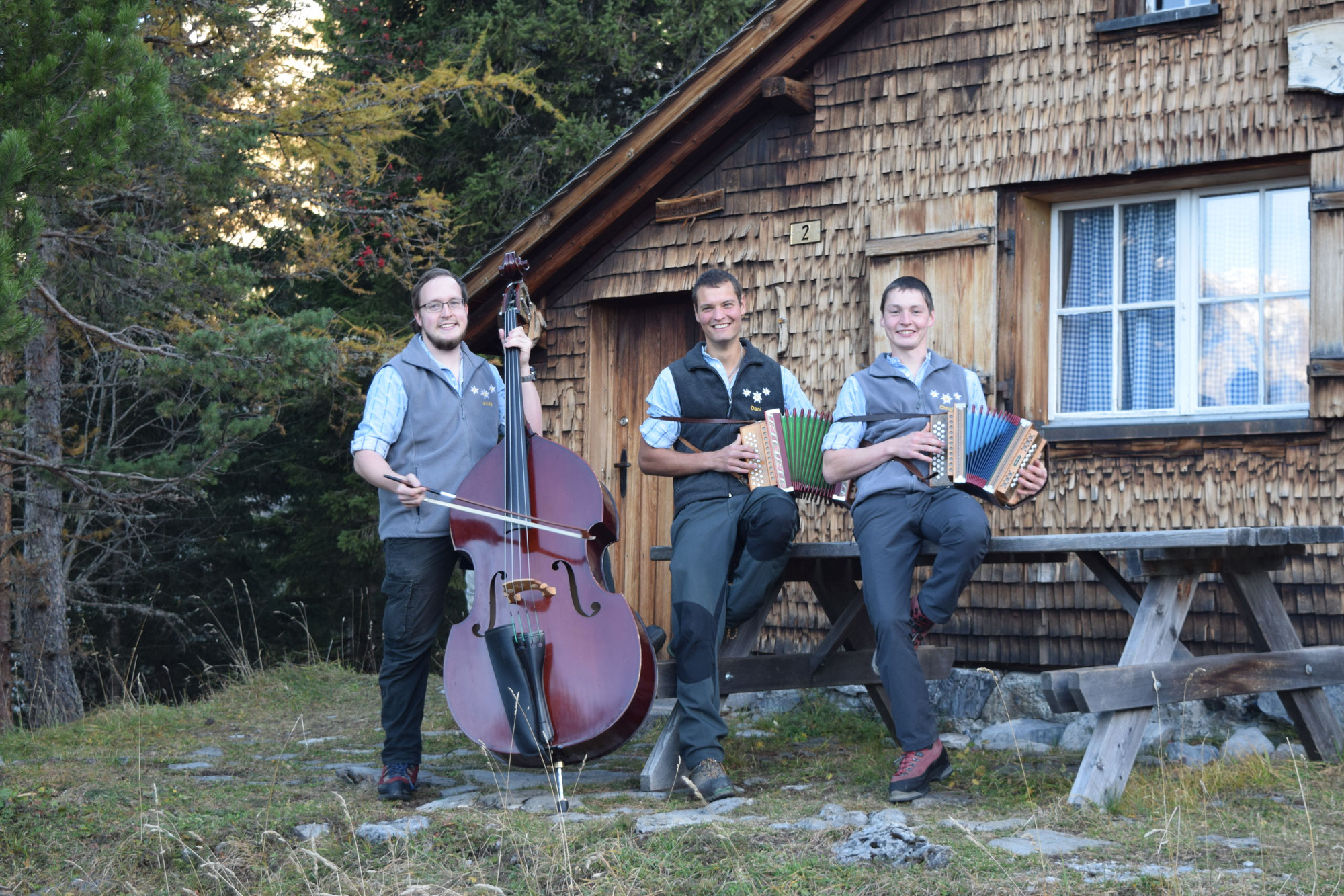 Echo vum Schilt zu dritt mit Kontrabass und Schwyzerörgeli vor einer Alphütte
